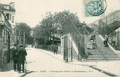 « 1904 : la passerelle de la rue de la Mare ; l'entrée des bureaux de la gare est cachée, au deuxième plan du cliché, par des arbres ; au fond, l'escalier montant vers la rue des Couronnes. »